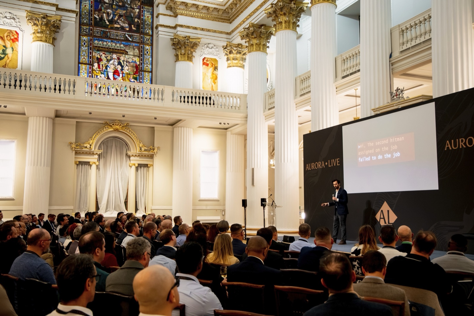 Carl Miller delivering a keynote on the digital underworld to an executive audience in a grand London hall